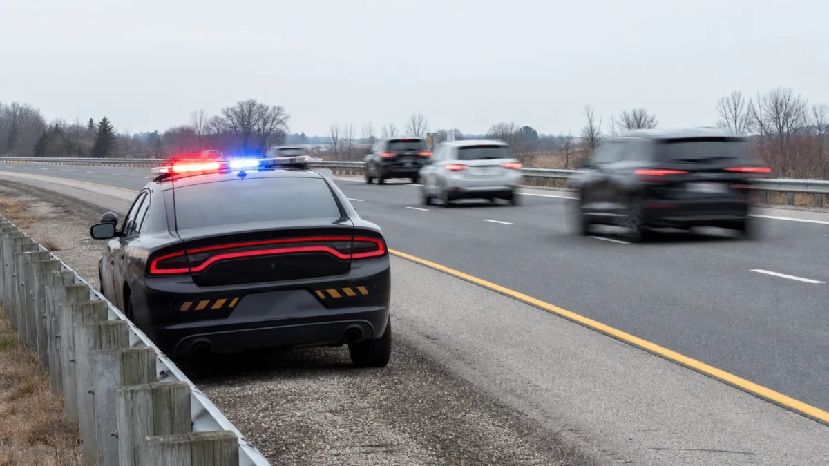 A stopped police cruiser with flashing lights on an Ontario highway shoulder as traffic moves into the far lane.